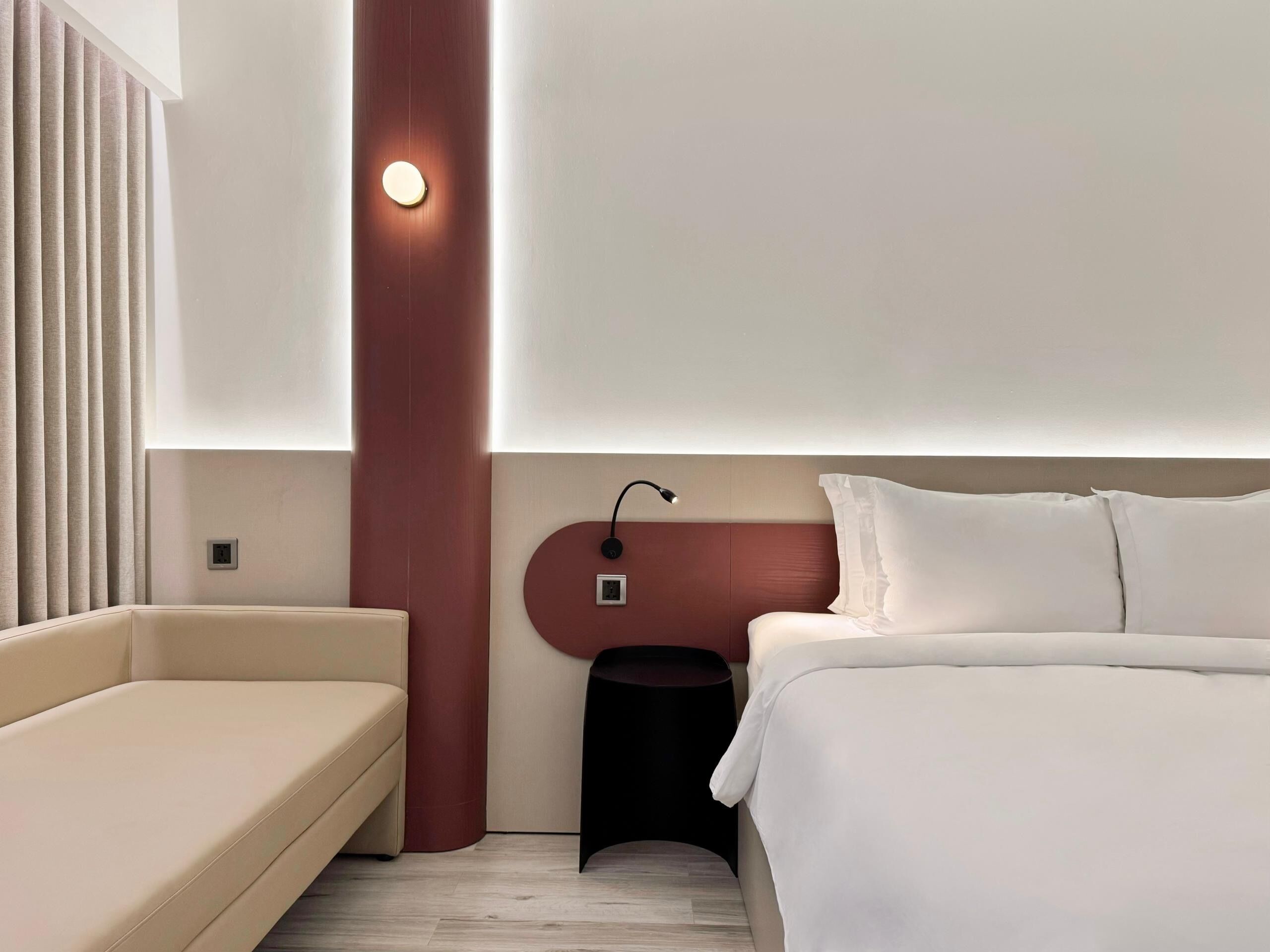 Una habitación de hotel moderna con una cama, un sofá, una mesita de noche y una lámpara de pared.