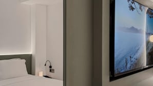 Ein modernes Hotelzimmer mit einem großen Bett, einem Nachttisch, einem wandmontierten Fernseher und Blick auf eine verschneite Landschaft.