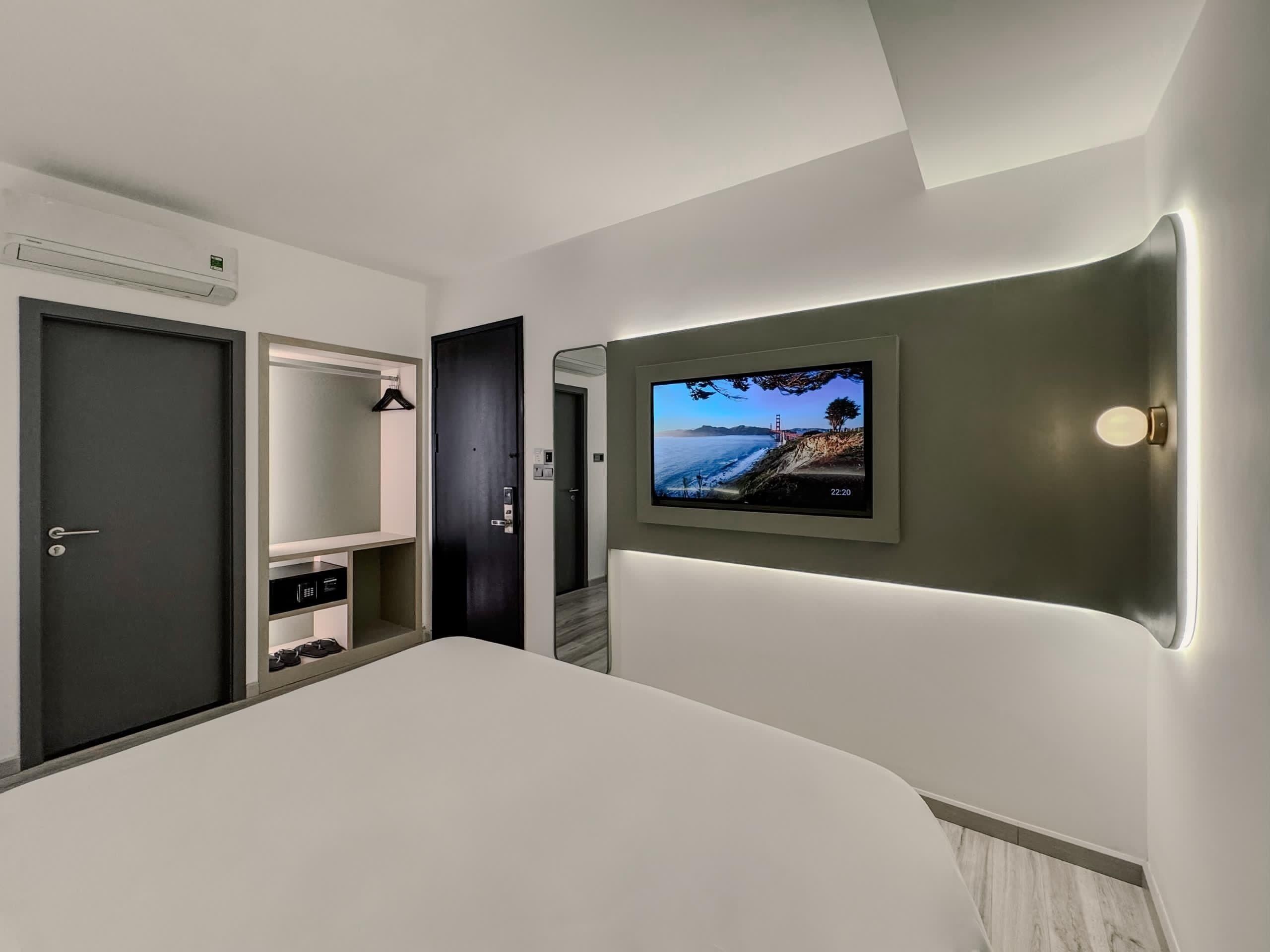 Una habitación de hotel moderna con una cama grande, un televisor montado en la pared, un armario y una puerta.