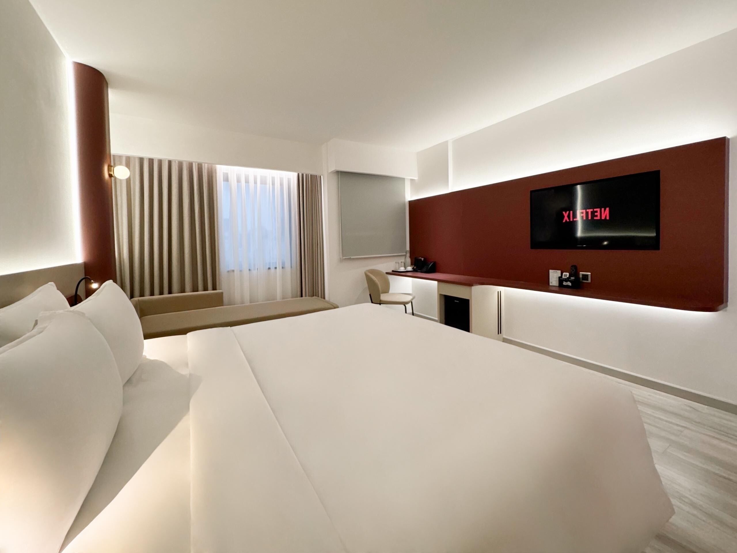 Een moderne hotelkamer met een groot bed, een bureau en een aan de muur bevestigde televisie.