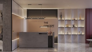 Ein Empfangsbereich mit modernem Design, der ein Empfangsschalter mit der Aufschrift "THE CONCEPT", eine schlichte Regaleinrichtung mit Dekoration und einen glatten, polierten Boden zeigt.