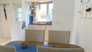A dining area with a wooden table, four wicker chairs, and a blue placemat. - Holiday Home 'Sylthus-Haithabu' with Private Terrace, Private Garden and Wi-Fi (Wenningstedt)