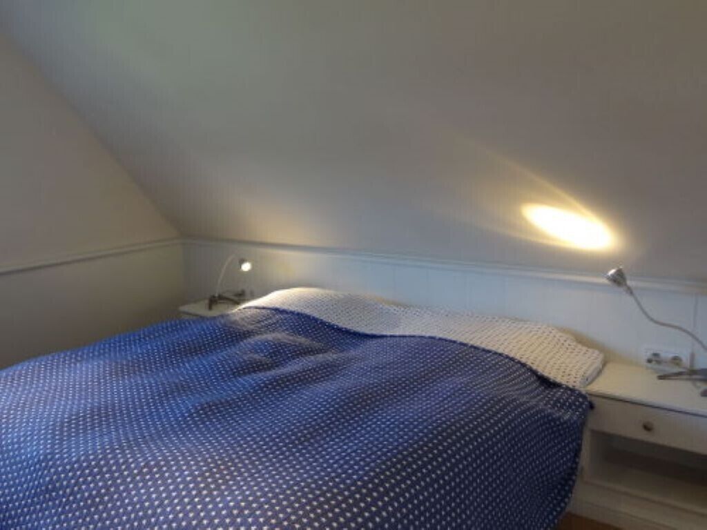 A bedroom with a bed, bedside table, lamp, and a wall-mounted light fixture.