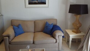 A beige sofa with blue cushions, a framed picture on the wall, and a lamp on a side table. - Holiday Home 'Sylthus-Haithabu' with Private Terrace, Private Garden and Wi-Fi (Wenningstedt)