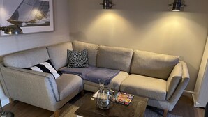 A living room with a grey sofa, patterned pillows, a coffee table with magazines, and wall-mounted lights. - Holiday Home 'Meerchenhaus' with Private Terrace, Garden, and Wi-Fi (Wenningstedt)