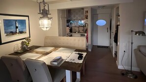 A modern dining area with a wooden table, white chairs, and a pendant light. A kitchen is visible in the background. - Holiday Home 'Meerchenhaus' with Private Terrace, Garden, and Wi-Fi (Wenningstedt)