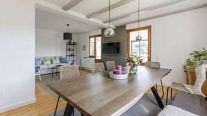 Una sala moderna con comedor, vigas de madera en el techo, televisor y un ventanal grande.