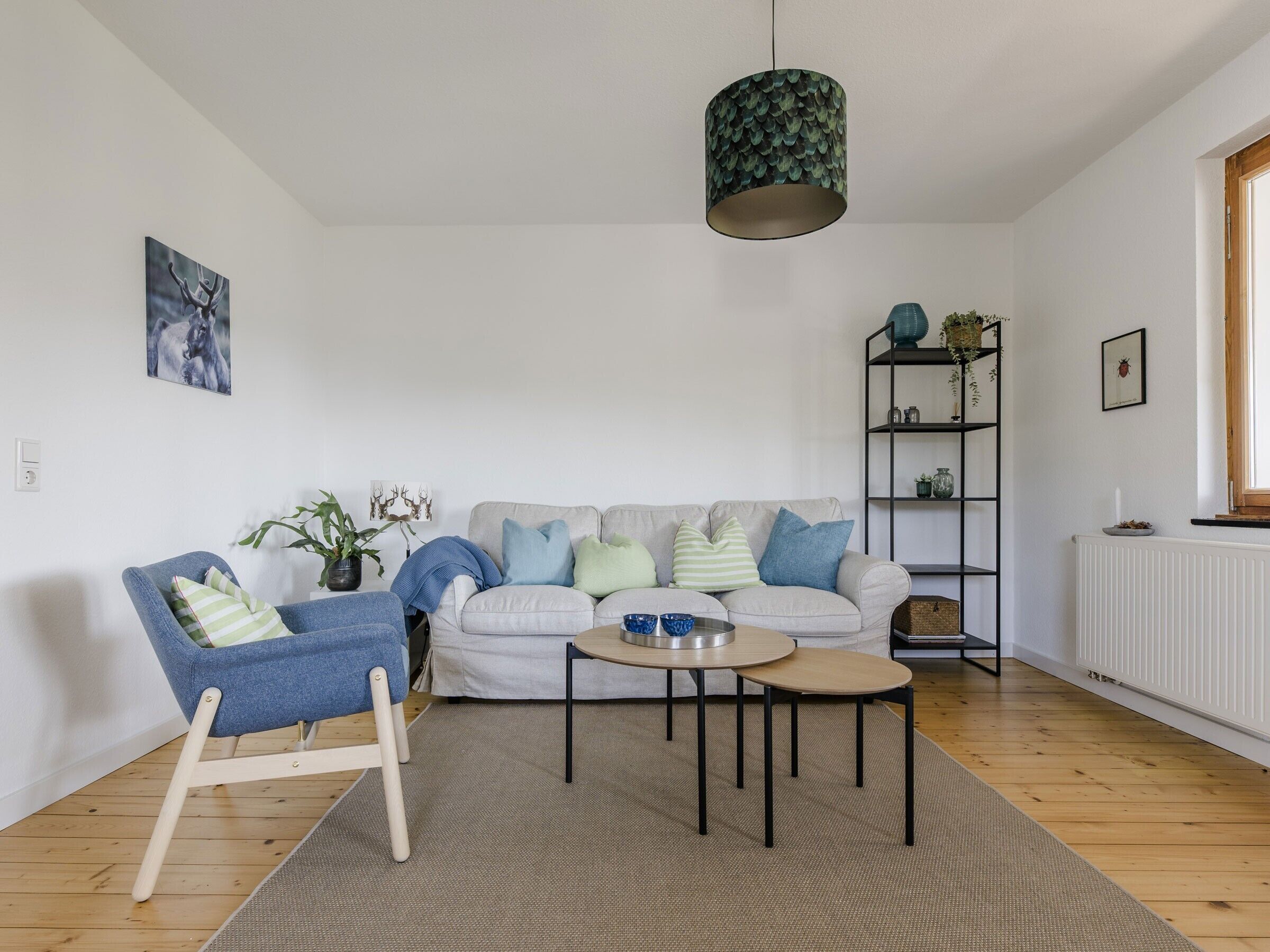 Uma sala de estar com sofá, poltrona, mesa de centro, estante e luminária pendente.