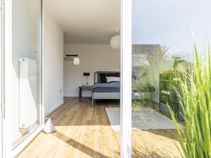 Un dormitorio con cama, mesita de noche, lámpara y vistas a través de un ventanal.