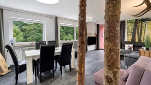 A modern interior with a dining area, a fireplace, and a view of the forest. - Apartment 'Villa Eichwald' with Shared Garden, Balcony and Wi-Fi (Freudenstadt)