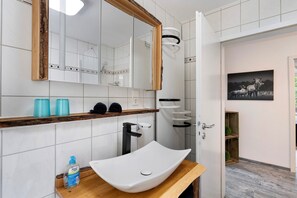 A bathroom with a white sink, a mirror, and a shower. - Apartment 'Villa Eichwald' with Shared Garden, Balcony and Wi-Fi (Freudenstadt)