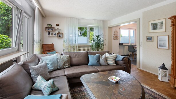 A living room with a brown leather sofa, a coffee table, and a view of a garden through a window. - Apartment 'Design Und Entspannug' with Private Terrace, Private Garden and Wi-Fi (Kandern)