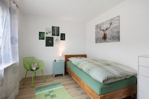 A bedroom with a bed, a chair, a nightstand, and wall art.