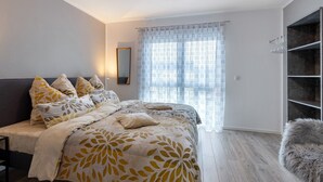 A bedroom with a bed, a mirror, a window with sheer curtains, and a wooden floor. - Apartment 'Haus Unterm Hohenstoffel' with Private Terrace and Wi-Fi (Hilzingen)