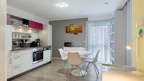 A modern kitchen with white cabinets, a microwave, and a coffee maker. There is a dining table with chairs and a painting on the wall. - Apartment 'Haus Unterm Hohenstoffel' with Private Terrace and Wi-Fi (Hilzingen)