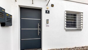 A black door with a handle, a window with horizontal blinds, and a small sign above the door. - Apartment 'Haus Unterm Hohenstoffel' with Private Terrace and Wi-Fi (Hilzingen)