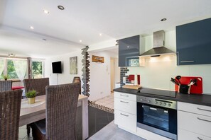 A modern kitchen with a built-in oven, a dining area with wicker chairs, and a TV mounted on the wall. - Apartment 'Langenwaldsee' with Private Terrace, Shared Garden and Wi-Fi (Freudenstadt)
