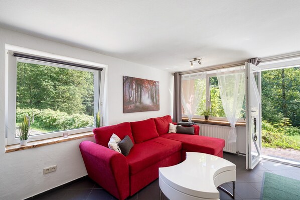 Una sala de estar moderna con un sofá sectional rojo, una mesa de centro blanca y grandes ventanales con vistas a zonas verdes.