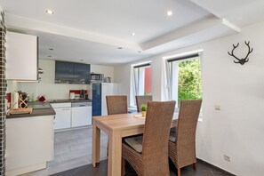 A modern kitchen with white cabinets, a dining area with wicker chairs, and a large window with a view of greenery. - Apartment 'Langenwaldsee' with Private Terrace, Shared Garden and Wi-Fi (Freudenstadt)