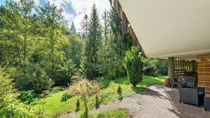 Eine Terrasse mit Gartenmöbeln, ein Pflasterweg und ein üppiger Garten mit verschiedenen Pflanzen und Bäumen.