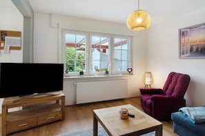 Uma sala de estar com televisão, mesa de centro, uma cadeira e uma janela com vista.
