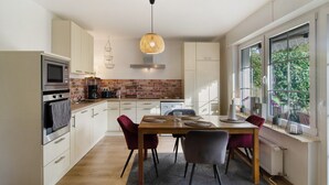 A modern kitchen with white cabinets, a brick backsplash, and a dining area with a wooden table and chairs.