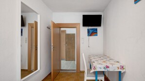 A room with a wooden door, a table with a floral tablecloth, a chair, a television mounted on the wall, and a wooden floor. - Holiday Home 'Haus Steinheim' with Shared Terrace, Garden, and Wi-Fi (Dillingen an der Donau)