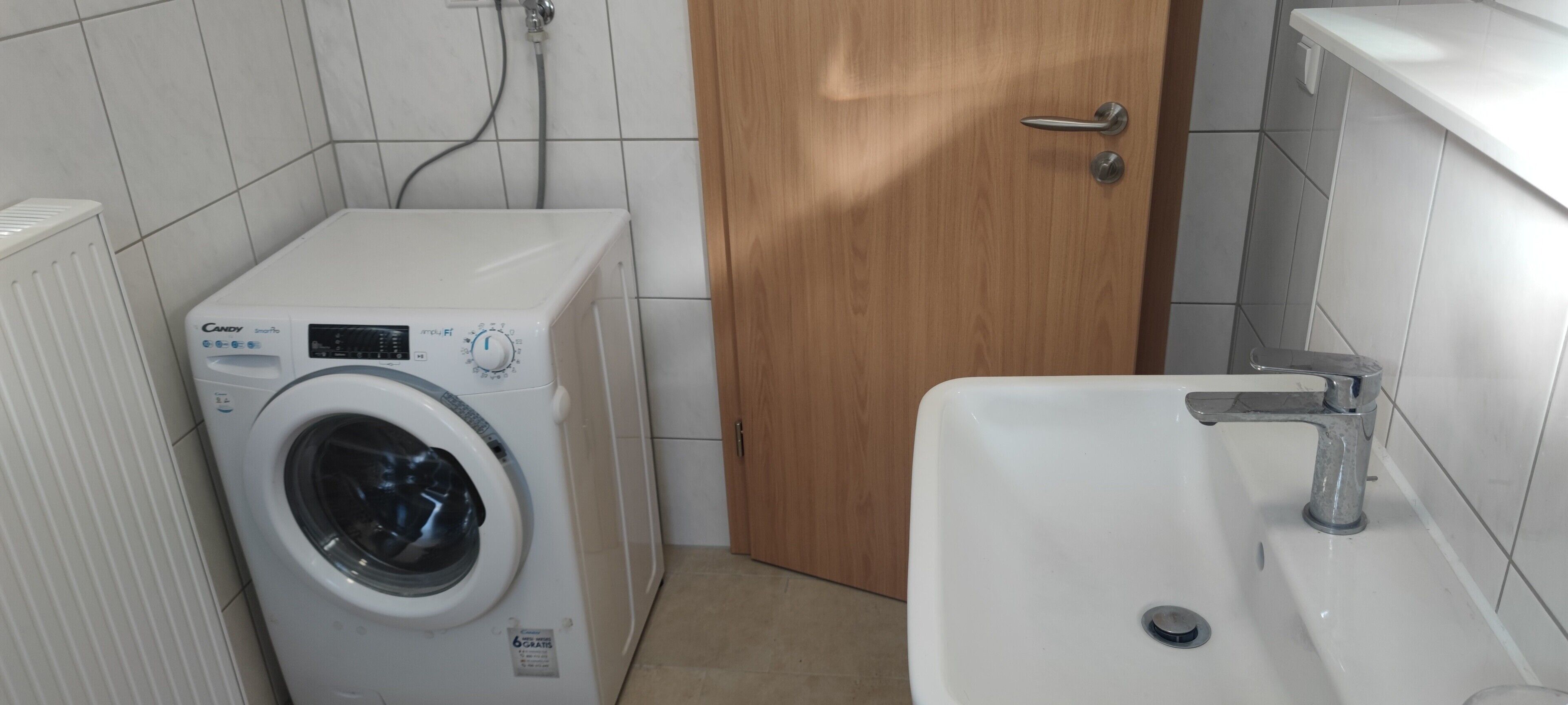 A compact bathroom with a white washing machine, a wooden door, and a white sink.