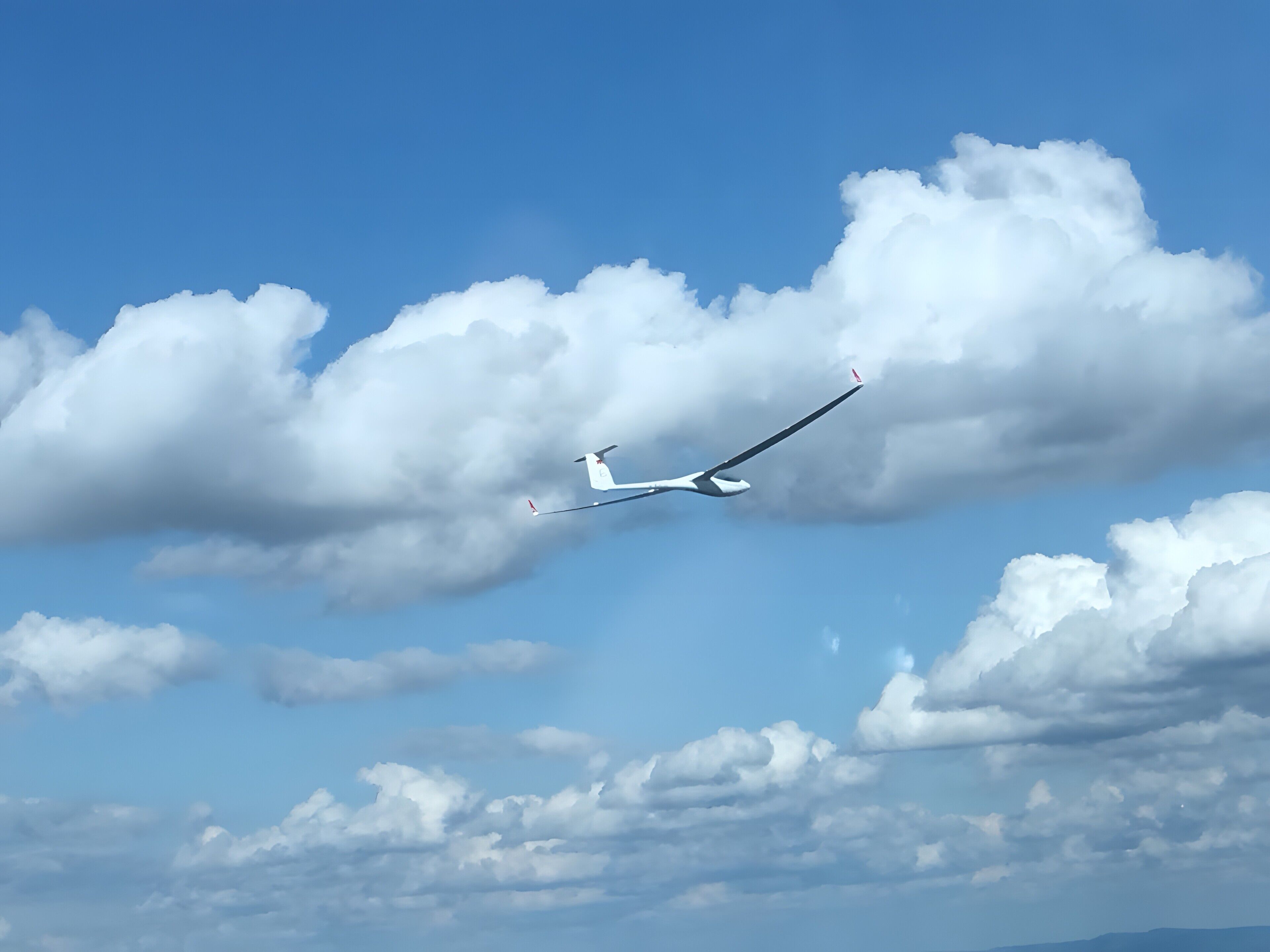 A glider in flight with a clear sky and scattered clouds.