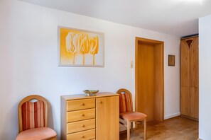 Une pièce comprenant une commode en bois, deux chaises, une porte et un tableau accroché au mur.