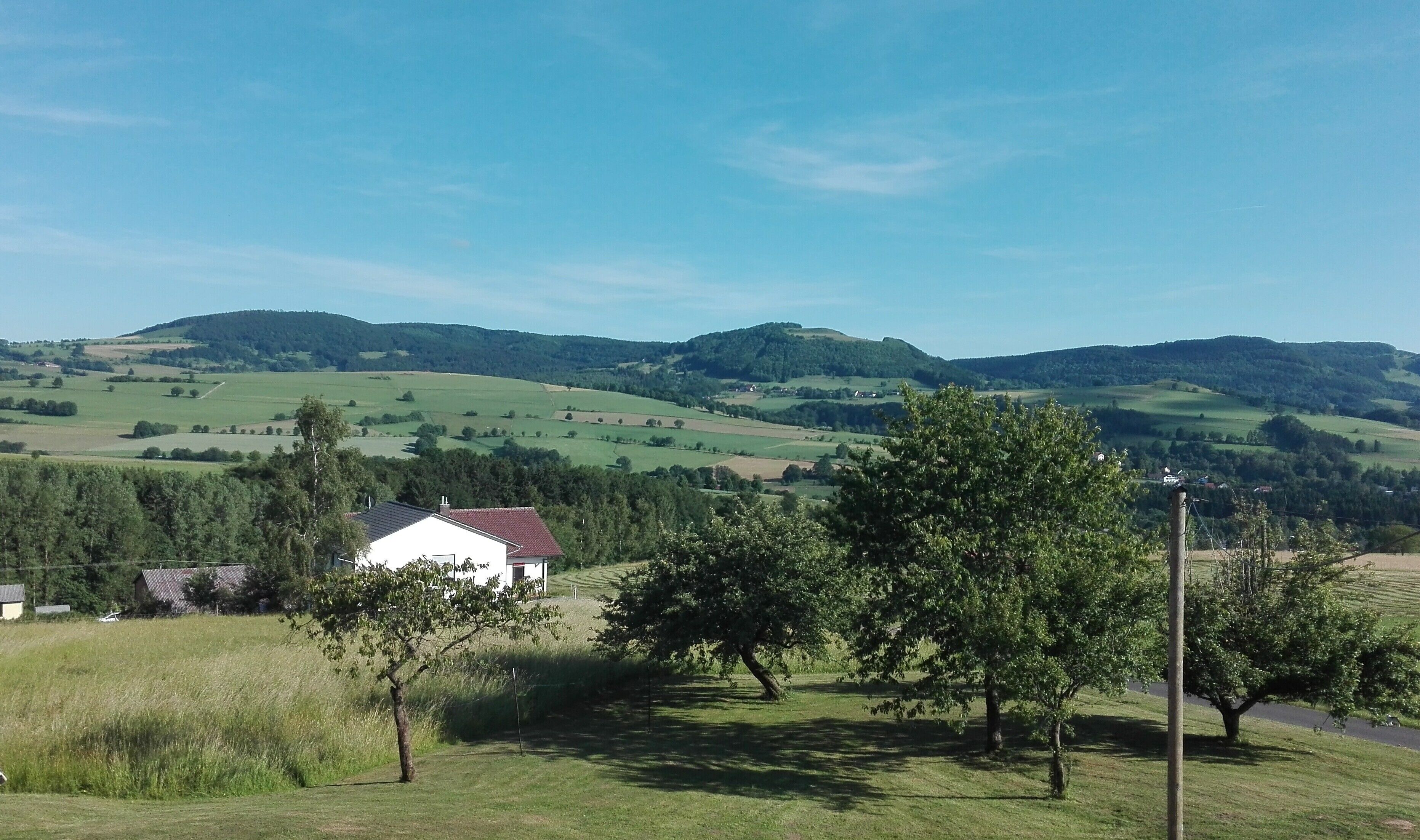 A rural landscape with rolling hills, a white building with a red roof, and a clear blue sky.