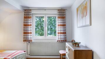 Ein Schlafzimmer mit einem Bett, einem Schminktisch, einem Stuhl, einem Fenster mit Vorhängen, einer Heizung und einem Bild an der Wand.