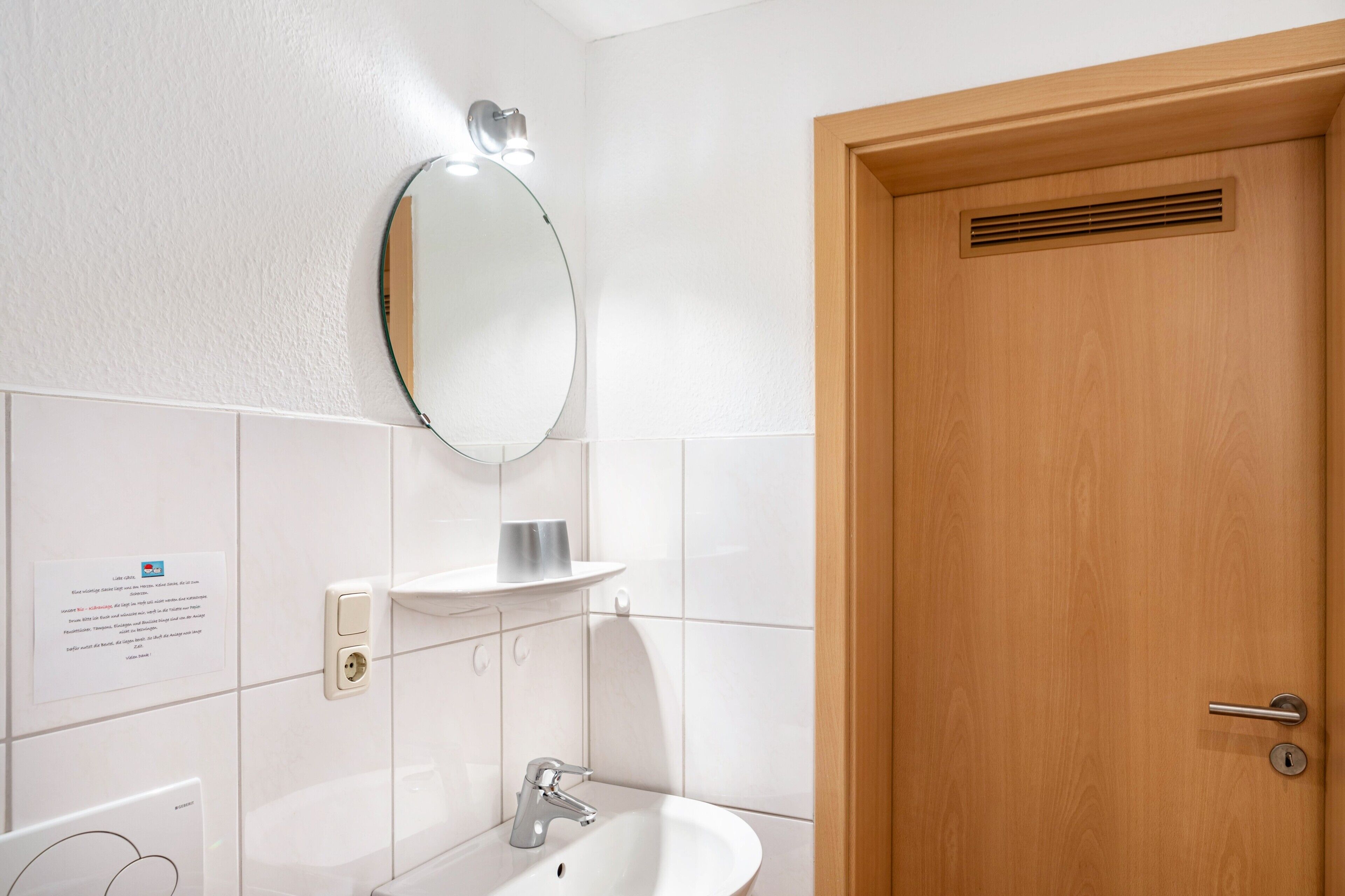 Un bagno con un lavandino bianco, uno specchio, un lampadario e una porta in legno.