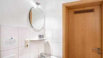 Un bagno con un lavandino bianco, uno specchio, un lampadario e una porta in legno.