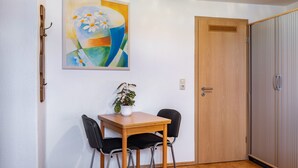 Ein Zimmer mit Holztür, einem Wandbild, einem kleinen Tisch mit zwei Stühlen und einem Blumentopf.