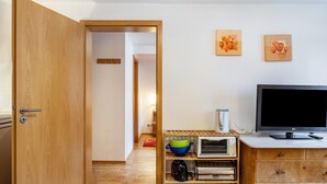 Ein Zimmer mit einer Holztür, einem Fernseher, einem Regal mit Küchenutensilien und einer Wand mit zwei gerahmten Bildern.