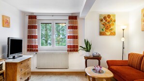 Ein Wohnzimmer mit Fernseher, Sofa und einem Vorhangfenster.