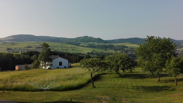 Ländliche Landschaft mit sanften Hügeln, einem weißen Haus und einem grünen Feld.