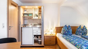 Ein gemütlicher Raum mit Kochnische, einem Bett mit gemusterten Betttextilien und einem Nachttisch mit Lampe.