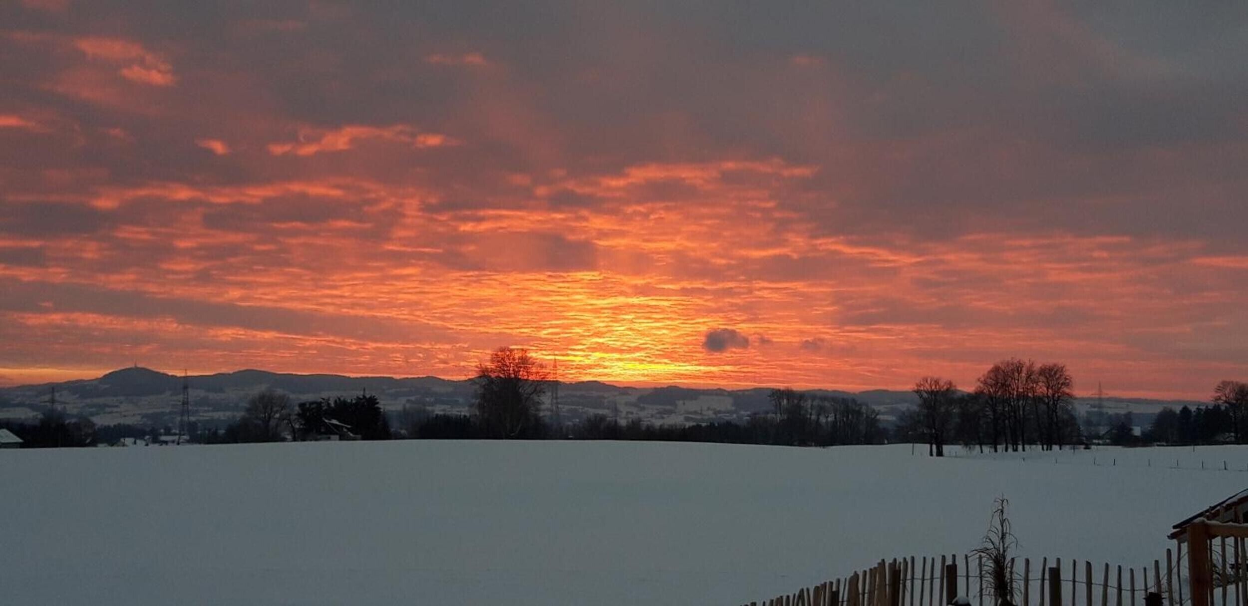 Ein Sonnenuntergang über einer verschneiten Landschaft mit einem fernen Gebirgszug.