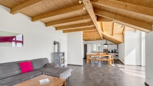 A spacious living area with a wooden ceiling, a gray sofa, a wooden coffee table, and a kitchen in the background. - Holiday Apartment 'Cosy Home Allgäu' with Mountain View, Balcony and Wi-Fi (Haldenwang)