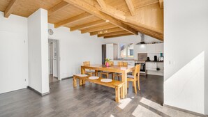 A spacious dining area with a wooden table and benches, a kitchen in the background, and a high ceiling with exposed beams. - Holiday Apartment 'Cosy Home Allgäu' with Mountain View, Balcony and Wi-Fi (Haldenwang)