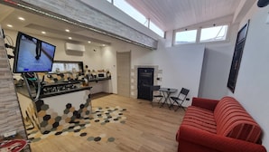 Una sala de estar moderna con un sofá rojo, una zona de cocina con televisor, y un comedor con mesa y sillas.