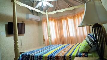 A room with a bed, a ceiling fan, a television, and a window with curtains.