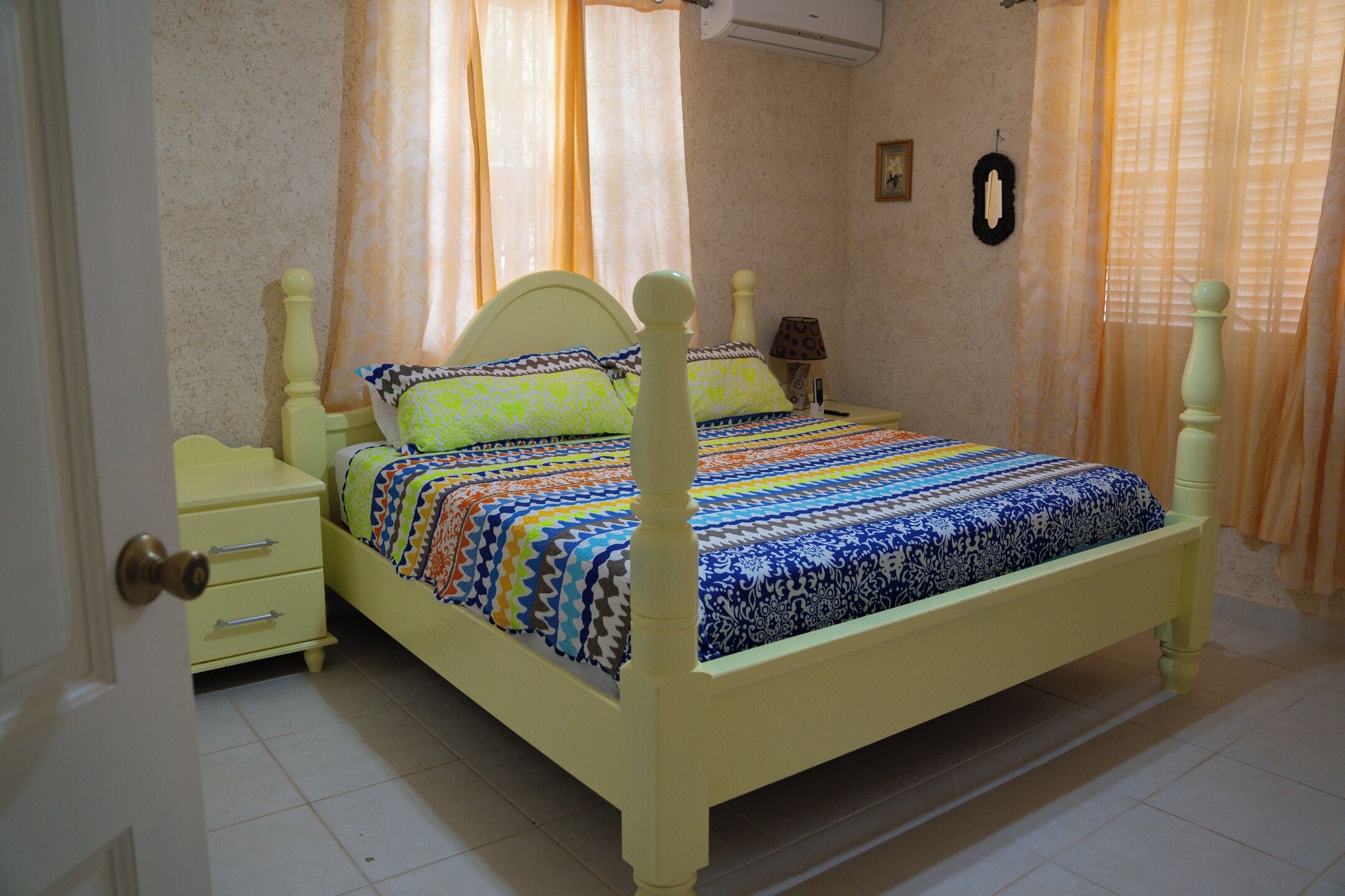 Una cama con una colcha estampada, una mesita de noche, una lámpara y cortinas.