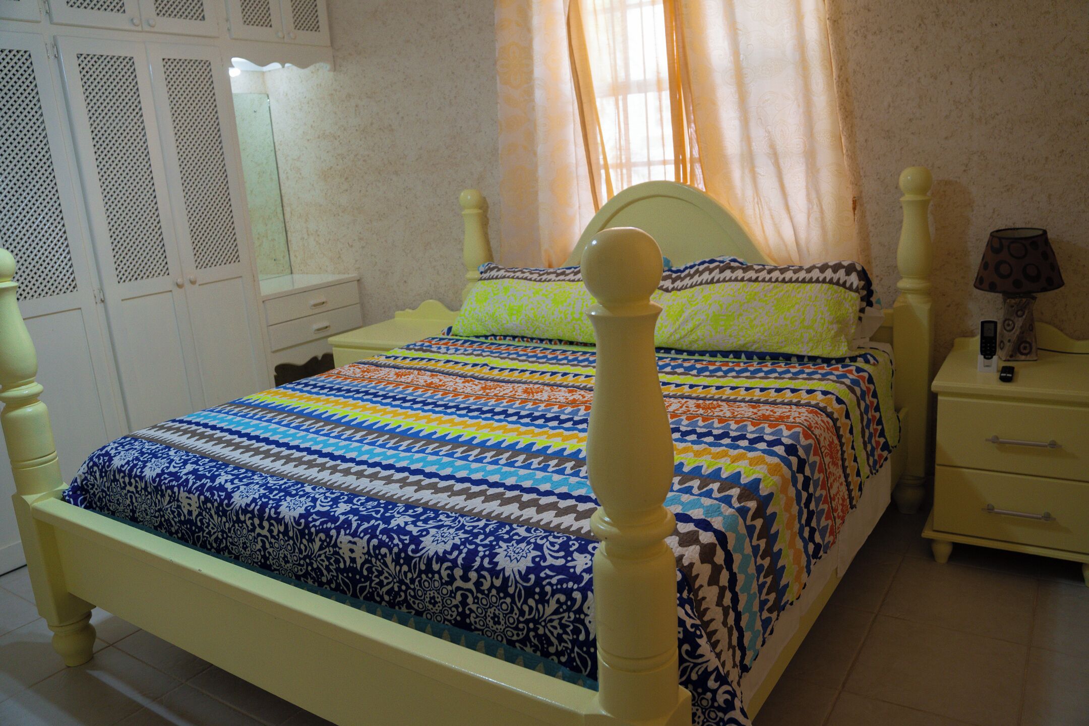 A bed with a patterned bedspread, a bedside table with a lamp, and a wardrobe with a mirror.