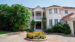 A large, two-story building with a white facade, a balcony, and a tiled roof. - Marzalea - by Zenbreak (Paynes Bay)