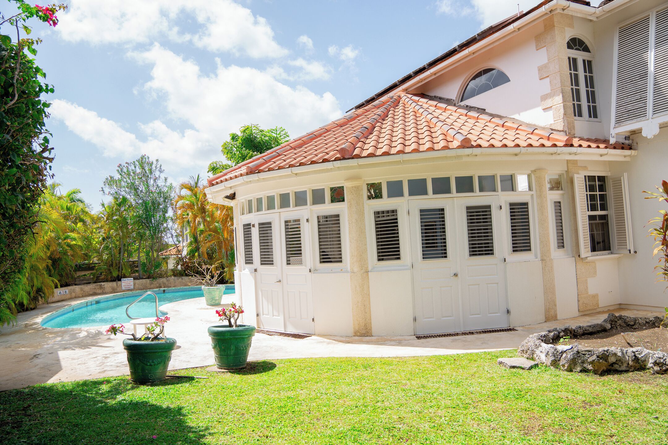 A house with a swimming pool, a covered patio, and a well-maintained lawn.