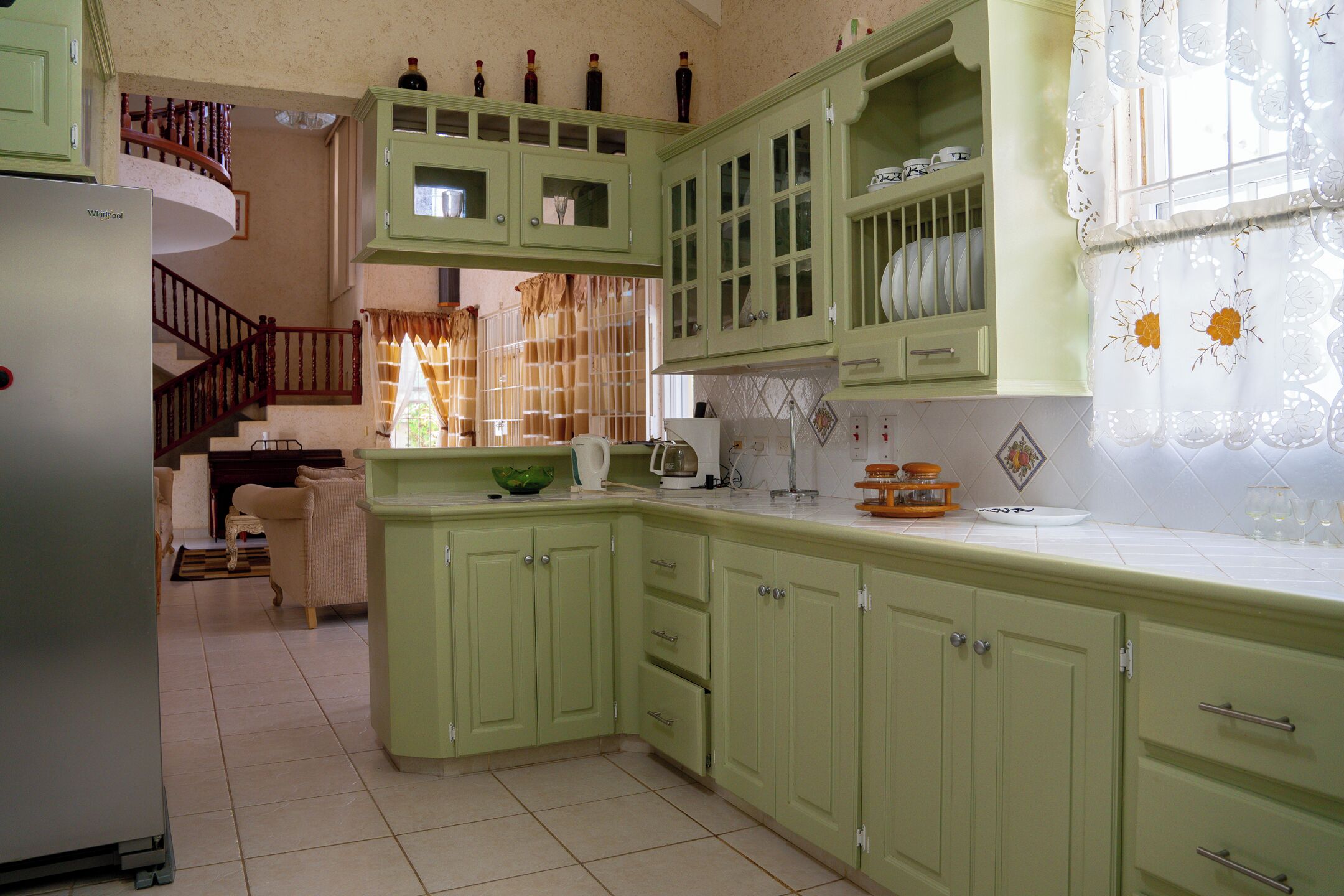 Una cocina con gabinetes verdes, un refrigerador y una escalera que lleva a un balcón.