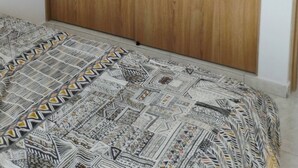 Un dormitorio con un armario de madera, una colcha estampada y una pared lisa.